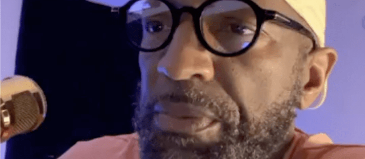 Man speaking into microphone, wearing glasses.